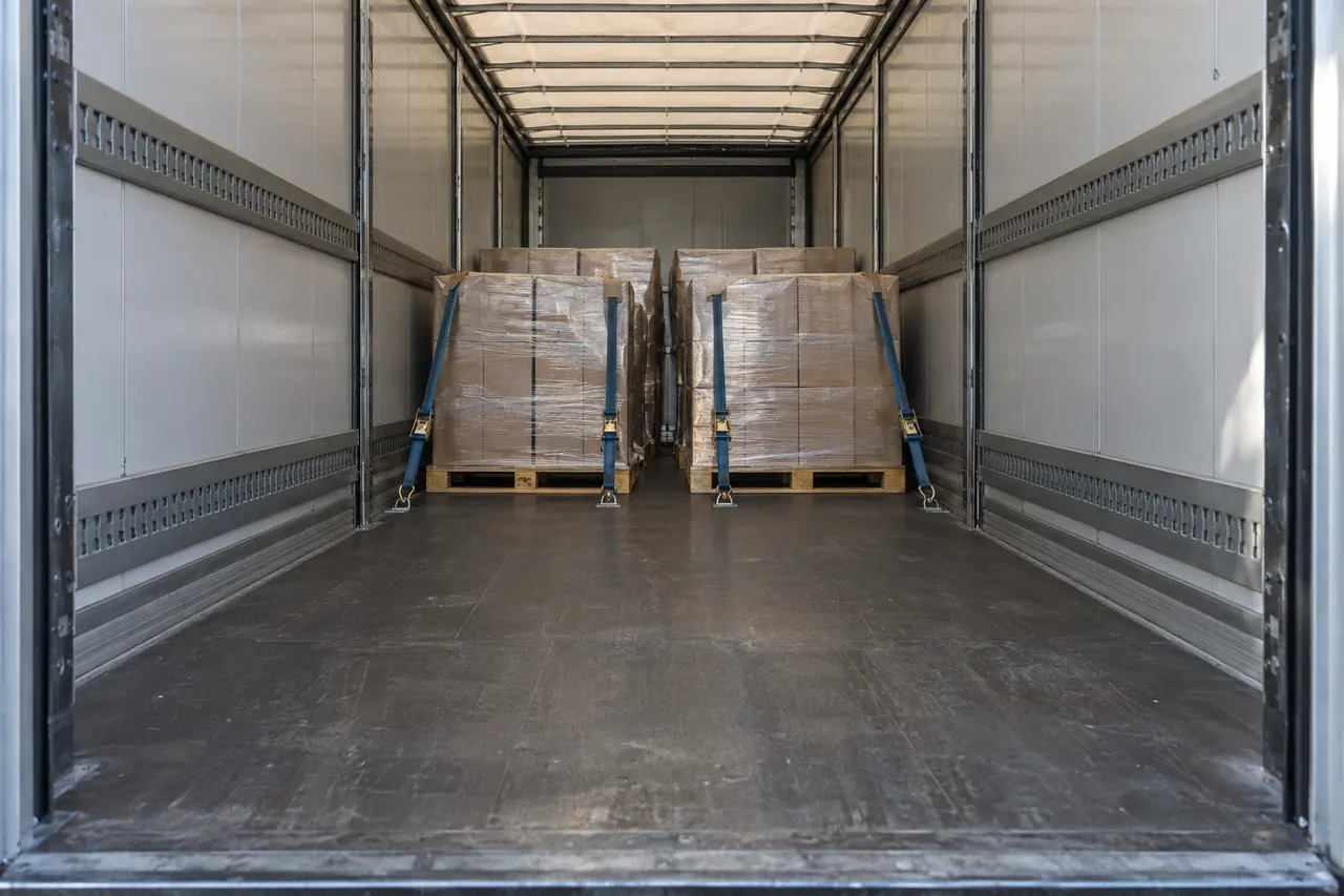 Palets bien trincados dentro de un tráiler a medio cargar, con luz natural entrando por las puertas.